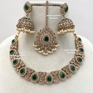 May include: An antique gold-toned jewelry set featuring a necklace, earrings, and a headpiece. The set is adorned with emerald green teardrop-shaped stones and small white pearls. The text "IndoExquisite Designs" is visible.