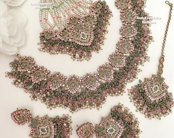 May include: A complete jewelry set featuring a necklace, earrings, headpiece, and a nose ring. The set is adorned with pink and green beads, pearls, and intricate metalwork. The design includes the text "IndoExquisite Designs".