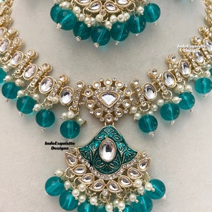 May include: A green and gold necklace with a large pendant featuring intricate designs and clear stones. The necklace is adorned with green glass beads and white pearls.