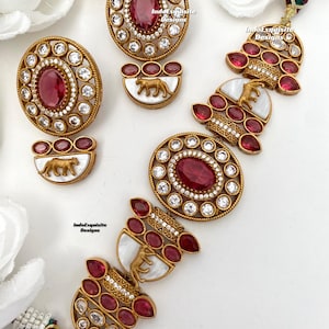 May include: A gold necklace featuring a tiger and lion design, with red and white stones. The necklace is made of metal and has a traditional Indian design.