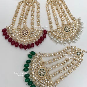 May include: Gold-toned headpieces with intricate detailing. Each piece features a central design with surrounding embellishments and dangling beads in red, white, and green. The headpieces are adorned with small, round, white pearls.