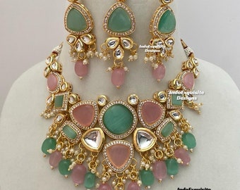 Puede incluir: Un conjunto de joyas dorado que incluye un collar, pendientes y una diadema. El conjunto incluye piedras preciosas verdes y rosas, detalles blancos y pequeñas cuentas perladas. El texto "IndoExquisite Designs" es visible.
