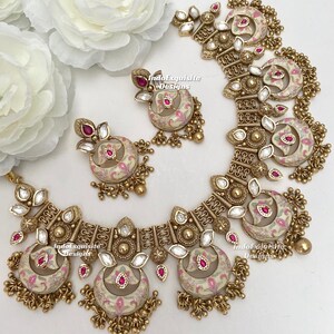 Pu&ograve; includere: Un set di gioielli color oro composto da collana e orecchini. Il set include una collana con pi&ugrave; pendenti a forma di mezzaluna e orecchini abbinati. Ogni pezzo ha una base color crema con motivi floreali rosa e accenti rossi. I gioielli sono impreziositi da cristalli trasparenti.