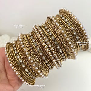 May include: A set of gold bangles with white pearl and rhinestone embellishments. The bangles are stacked on top of each other and have a shiny finish.