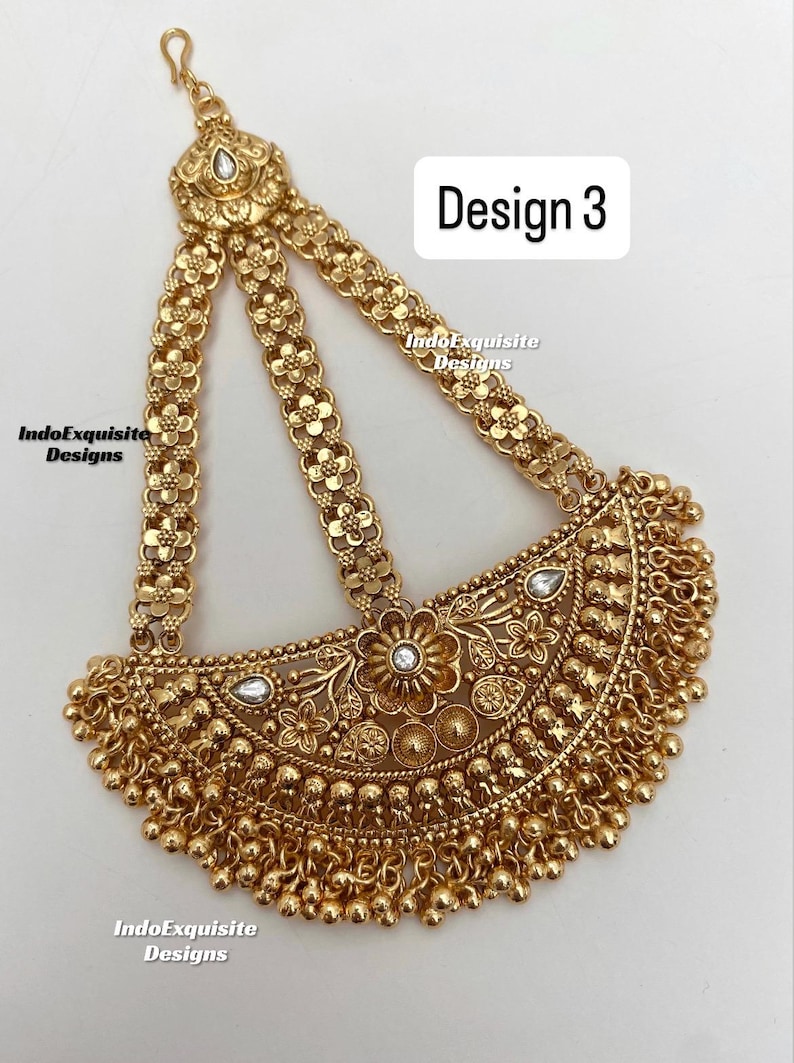 May include: A gold-toned headpiece featuring three floral-patterned chains connected to a semi-circular pendant with intricate embossed floral motifs, small white stones, and dangling gold beads. The text Design 3 and IndoExquisite Designs are visible.