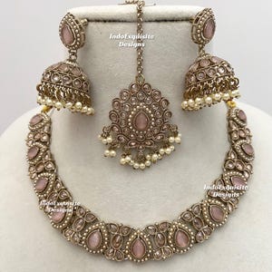 May include: A complete jewelry set featuring a necklace, earrings, and a headpiece. The set is in a silver tone with pink gemstones and small white pearls. The text "IndoExquisite Designs" is visible on the jewelry.