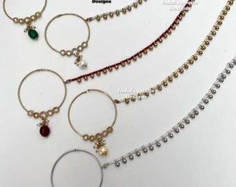May include: Four gold nose rings with dangling charms. The charms are a green stone, a red stone, a pearl, and a pearl. Each ring is attached to a chain with small gold beads. The chains are green, red, gold, and silver.
