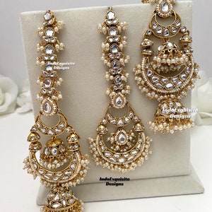 Puede incluir: Un conjunto de joyer&iacute;a en tono dorado que incluye dos pendientes largos y un adorno para la cabeza a juego, decorados con piedras claras reflectantes y peque&ntilde;as perlas blancas. Las piezas muestran metalister&iacute;a detallada.