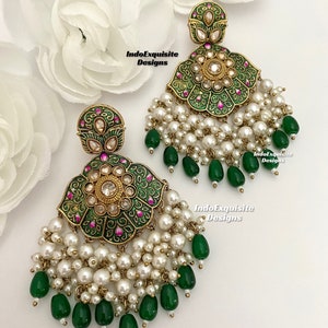 Peut inclure: Une paire de boucles d'oreilles vertes et dorées avec des accents de perles blanches et de pierres précieuses vertes. Les boucles d'oreilles présentent un motif floral avec des détails complexes. IndoExquisite Designs est imprimé sur l'image.