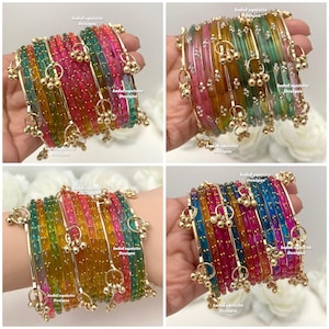 May include: A set of colourful bangles with gold-coloured accents and small dangling charms. The bangles are in shades of pink, green, blue, and yellow. The text "IndoExquisite Designs" is visible on the image.