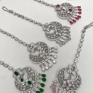 May include: Four silver-toned maang tikka headpieces featuring crescent-shaped pendants adorned with clear crystals and dangling teardrop-shaped stones in red, pink, green, and mint. Each piece includes a delicate chain with a hook attachment.