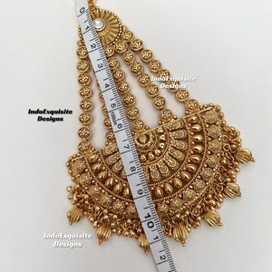 May include: A gold-toned headpiece featuring a central semi-circular pendant with intricate embossed patterns and dangling beads, attached to three chains with circular links. A measuring tape shows a length of approximately 4.5 inches.