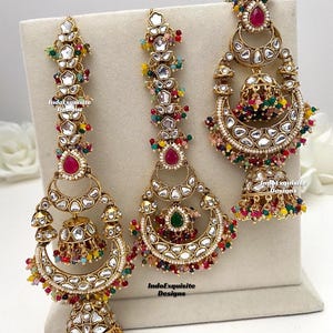 Puede incluir: Tres pendientes dorados con intrincados trabajos en metal, piedras transparentes y cuentas de colores. Los dise&ntilde;os incluyen formas de media luna, elementos en forma de campana y piedras centrales en forma de l&aacute;grima en rosa y verde, marcados IndoExquisite Designs.