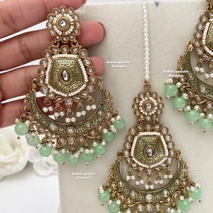 May include: A set of gold-tone earrings, a necklace, and a maang tikka with green and white accents. The jewellery features intricate designs and is adorned with pearls and green beads.