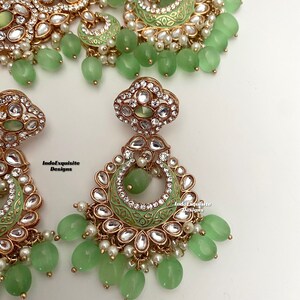 May include: A green and gold Indian bridal necklace set with matching earrings. The necklace features a delicate design with pearls and green stones. The earrings are long and dangle with green stones and pearls.
