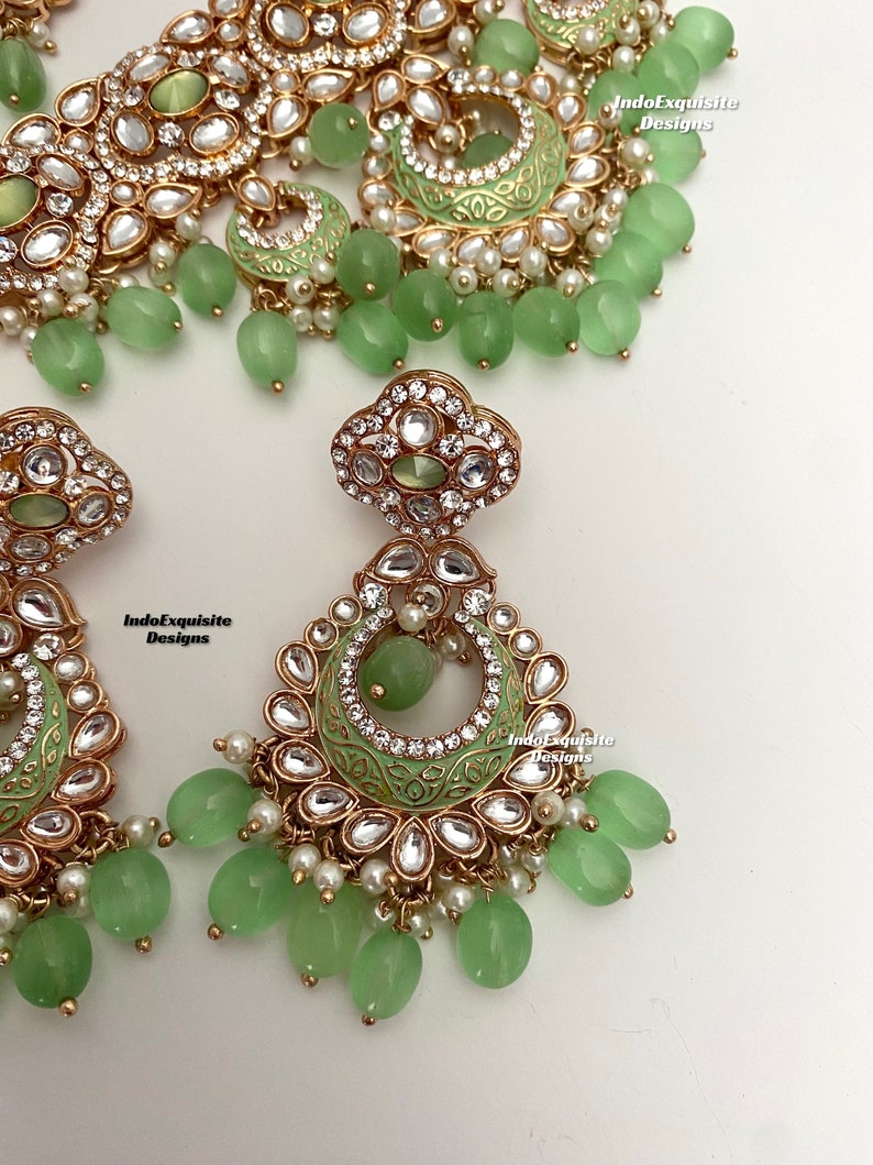 May include: A green and gold Indian bridal necklace set with matching earrings. The necklace features a delicate design with pearls and green stones. The earrings are long and dangle with green stones and pearls.