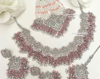 May include: A silver and pink bridal jewelry set with a necklace, earrings, a maang tikka, and a nose ring. The set features intricate designs with pink beads and clear stones.