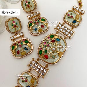 Puede incluir: Un conjunto de joyas dorado con collar y pendientes. Las piezas tienen un fondo verde claro con diseños florales coloridos y están acentuadas con pequeñas piedras transparentes y perlas. El texto "More colors" es visible.