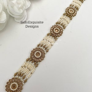 May include: A gold and white beaded hair chain with four decorative floral accents. The chain has a hook clasp.