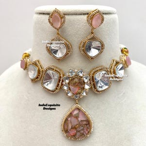 Peut inclure: Un collier en or avec un pendentif en pierres précieuses roses et blanches. Le collier présente une rangée de pierres précieuses de forme carrée avec une pierre précieuse plus grande en forme de larme au centre. Le collier est accompagné d'une paire de boucles d'oreilles assorties avec des pierres précieuses roses et blanches.