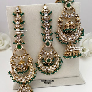 Puede incluir: Un conjunto de joyer&iacute;a en tono dorado que incluye dos adornos verticales largos para el cabello y un par de pendientes a juego. Cada pieza est&aacute; decorada con piedras blancas, detalles en forma de gota verdes y peque&ntilde;as cuentas verdes. Texto IndoExquisite Designs.