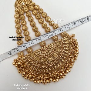 May include: A gold-toned headpiece featuring a semi-circular pendant with intricate floral engravings and dangling beads, connected to four vertical chains of small circular discs. A measuring tape shows the piece is approximately 7.5 inches long.