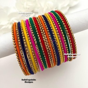 Può includere: Un set di braccialetti di velluto colorati con perline dorate. I braccialetti sono in tonalità di rosso, arancione, giallo, verde, blu e rosa.