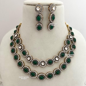 Peut inclure: Un collier à deux rangs et des boucles d'oreilles assorties avec des pierres vertes et des strass clairs. Le collier et les boucles d'oreilles sont dorés et de style vintage.