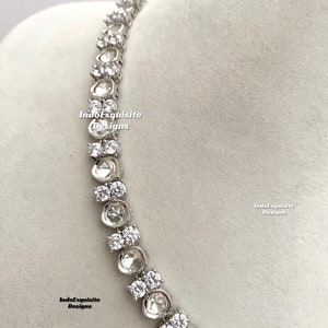 May include: A silver necklace with a row of clear, round stones. The stones are set in a silver setting and are connected by a silver chain. The necklace is on a white background.