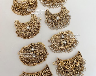 Puede incluir: Una colección de siete horquillas doradas con intrincados patrones florales y de cachemira en relieve. Varias horquillas están adornadas con pequeñas cuentas blancas y piedras transparentes. El texto IndoExquisite Designs es visible.