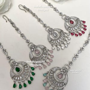 May include: Four silver-toned maang tikka headpieces featuring clear crystal accents and dangling teardrop-shaped stones in red, light pink, emerald green, and mint green. Each piece includes a hook for attachment and intricate metalwork.