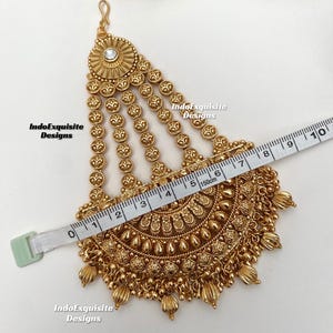 May include: A gold-colored headpiece with intricate floral and beaded designs. The headpiece is measured with a tape measure, showing a width of approximately 6 inches. The text "IndoExquisite Designs" is visible.