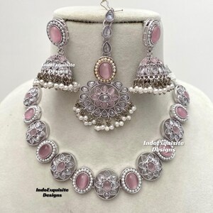 Op de afbeelding: Een zilveren en roze kettingset met een bijpassend paar oorbellen en een tikka. De ketting heeft een rij ronde roze stenen omgeven door zilveren filigraan en witte parels. De oorbellen en tikka hebben vergelijkbare ontwerpen.
