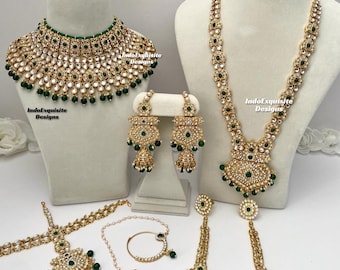 May include: A traditional Indian bridal jewellery set featuring a gold necklace, earrings, a maang tikka, a nose ring, and a set of bangles. The jewellery is adorned with white stones and green accents.