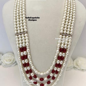 May include: A multi-strand pearl necklace with alternating sections of white pearls and red beads. The necklace has a rhinestone accent and is displayed on a white mannequin. The text "Design 6" is visible.