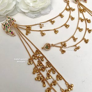 May include: Gold-coloured hair jewellery with dangling chains and small bell-shaped charms. The ornate pieces feature colourful gemstones and pearls. The text "IndoExquisite Designs" is visible on the image.
