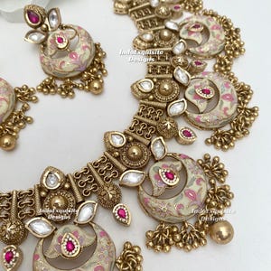 Pu&ograve; includere: Un set di collana e orecchini color oro. I gioielli presentano smalto color crema con disegni floreali rosa e accenti di pietre preziose rosse. Il set include perline dorate pendenti e pietre trasparenti a forma di goccia.