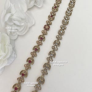 Może przedstawiać: Złoty łańcuszek z wzorem półksiężyca i przezroczystymi i czerwonymi kamieniami szlachetnymi. Łańcuszek leży na białym tle. Na zdjęciu widnieje napis IndoExquisite Designs.