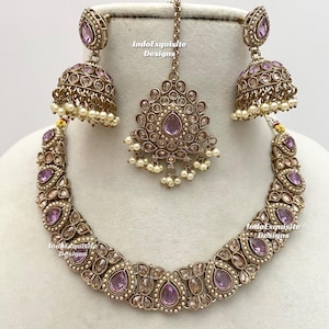 May include: An antique gold-toned jewellery set comprising a necklace, earrings, and a headpiece. The set features lavender gemstones and small white pearls. The earrings are bell-shaped, and the headpiece is a pendant.