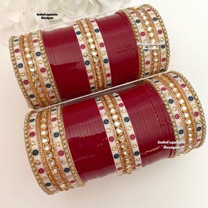 Può includere: Un set di braccialetti rossi e bianchi con decorazioni dorate e bianche. I braccialetti sono decorati con piccoli specchi rotondi e perle bianche. Il testo "IndoExquisite Designs" è visibile sui braccialetti.