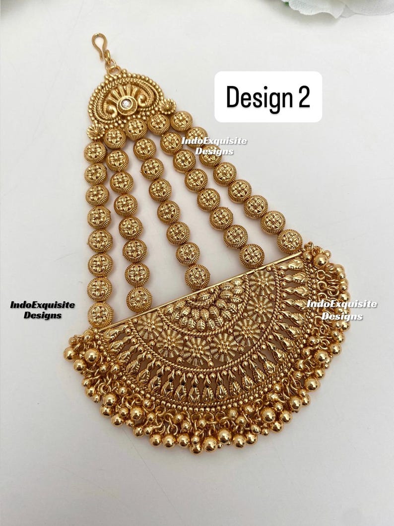 May include: Gold-toned headpiece with intricate floral and circular designs. The headpiece features multiple strands of small, round embellishments and a half-moon shaped central piece. The text "Design 2" is visible.