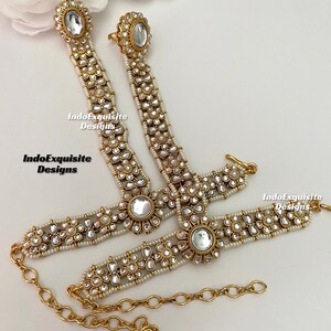 May include: A pair of gold anklets with white pearl and clear rhinestone embellishments. The anklets are connected by a gold chain.