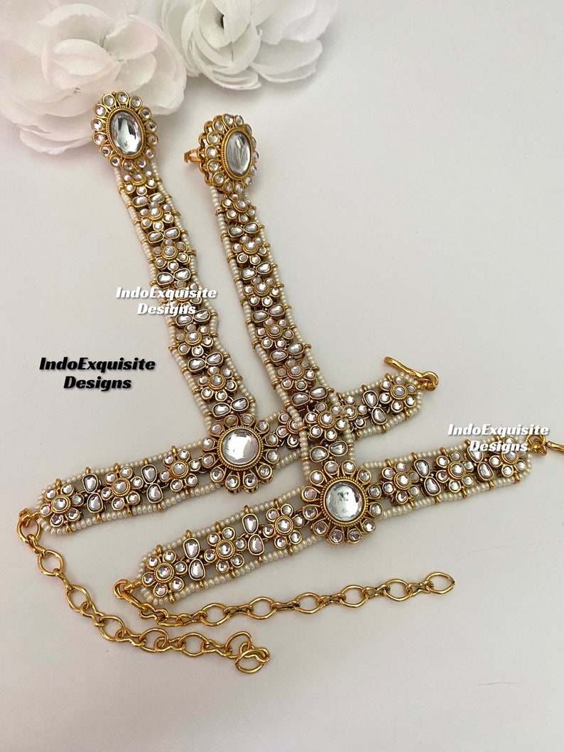May include: A pair of gold anklets with white pearl and clear rhinestone embellishments. The anklets are connected by a gold chain.