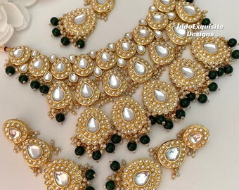 May include: A gold necklace and earrings set with teardrop-shaped pendants adorned with white pearls and green beads. The jewelry features intricate designs and a traditional Indian style.