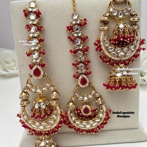 Puede incluir: Un conjunto de joyer&iacute;a etiquetado como Hot Pink que incluye dos grandes pendientes dorados y un adorno para la cabeza a juego. Cada pieza est&aacute; decorada con piedras claras, piedras rojas en forma de l&aacute;grima y peque&ntilde;as cuentas rojas, con formas de media luna y colgantes jhumka.