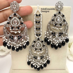 May include: A set of silver earrings and a matching maang tikka, featuring black and white stones and pearls. The earrings have a crescent moon shape with dangling black beads. The maang tikka has a similar design with a long chain of pearls.