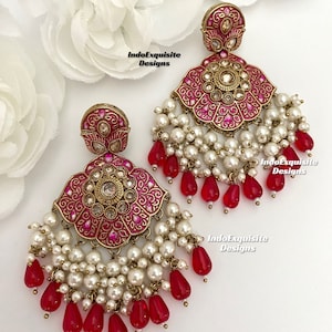 May include: A pair of pink and gold earrings with pearl and red teardrop accents. The earrings feature a floral design with intricate details. IndoExquisite Designs is printed on the image.