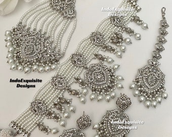 Op de afbeelding: Een zilveren en witte parel bruids kettingset met een choker, oorbellen en een maang tikka. De set heeft ingewikkelde zilveren ontwerpen met witte parels.