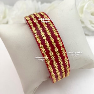 May include: A set of red bangles with gold floral patterns, stacked on a white pillow. The text "IndoExquisite Designs" is visible on the bangles.
