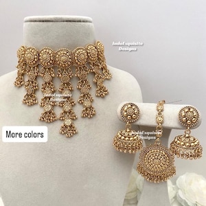 Könnte beinhalten: Ein goldfarbenes Schmuckset mit einer Halskette und passenden Ohrringen. Die Halskette und die Ohrringe haben ein detailliertes, verziertes Design mit hängenden Elementen. Das Set wird auf einem Schaufensterkopf präsentiert, mit dem Text "More colors".